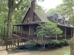 Eine Holzhütte mit Veranda und Schornstein, umgeben von Bäumen.