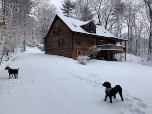 A wooden cabin with a porch, surrounded by snow-covered trees.