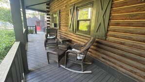 A wooden cabin with a porch featuring wicker furniture and a view of a red building in the distance. - Walk to Cushing Academy ! Sleeps 10 (Ashburnham)
