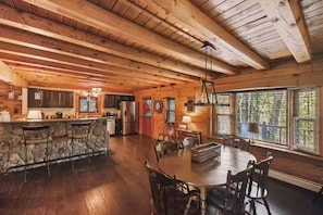 A spacious wooden cabin interior with a kitchen, dining area, and large windows.