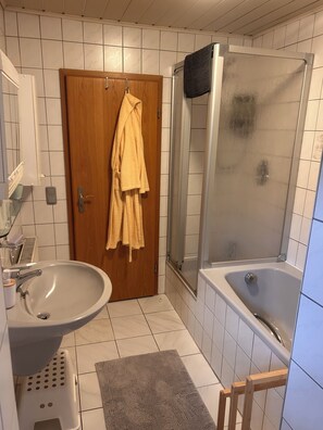 A bathroom with a sink, toilet, shower, and a wooden door. - Vrbo Property (Lohr am Main)