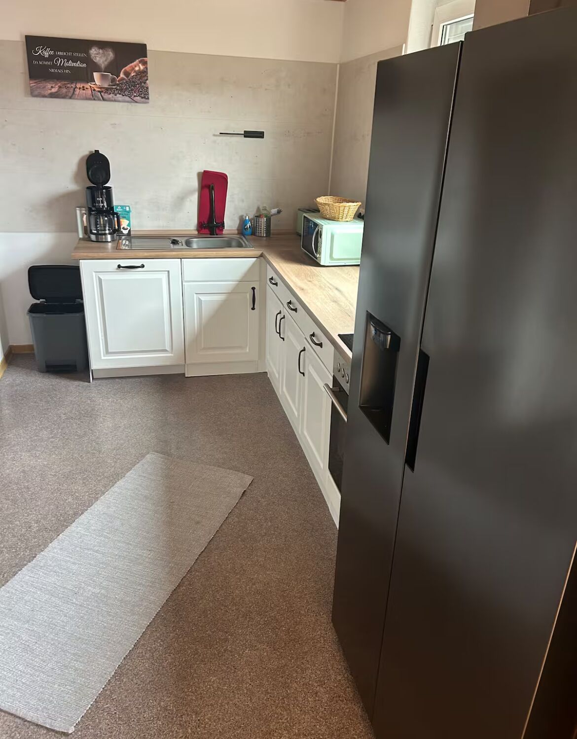 Eine kompakte Küche mit weißen Schränken, einem Edelstahlkühlschrank, einer Kaffeemaschine und einer Mikrowelle.