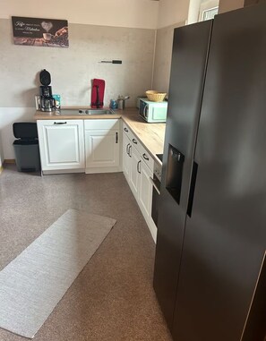 Eine kompakte Küche mit weißen Schränken, einem Edelstahlkühlschrank, einer Kaffeemaschine und einer Mikrowelle.