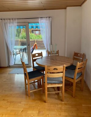 A dining area with a round wooden table and four chairs, a glass door leading outside, and a view of greenery. - Vrbo Property (Lohr am Main)