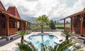 Uma piscina com vista para campos em socalcos, edifícios de madeira com designs elaborados e uma palmeira no centro.