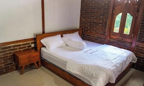 A neatly made bed with white linens in a room with brick walls and a wooden door. - Instay Villa Dieng Kademangan (Wonosobo)