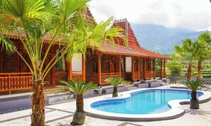 A traditional wooden building with a red roof, a swimming pool, and palm trees. - Instay Villa Dieng Kademangan (Wonosobo)