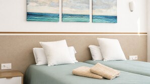 Ein Hotelzimmer mit einem Bett, zwei Kissen, einer Decke und zwei an der Wand befestigten Bildern einer Strandansicht.
