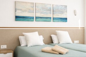 Een hotelkamer met een bed, twee kussens, een deken en twee aan de muur bevestigde schilderijen van een strandgezicht.