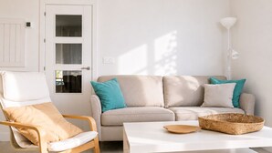 Ein Wohnzimmer mit einem beigefarbenen Sofa, einem Holzstuhl, einem weißen Couchtisch und einem gewebten Korb.