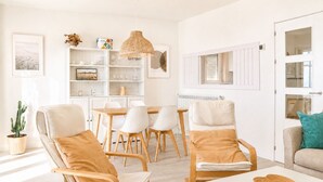 Ein modernes Wohnzimmer mit Essbereich, weißen Möbeln, einer Kakteenpflanze und einer Pendelleuchte.