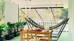 Una silla hamaca, una mesa de madera y plantas en macetas en una habitación con vista a árboles.