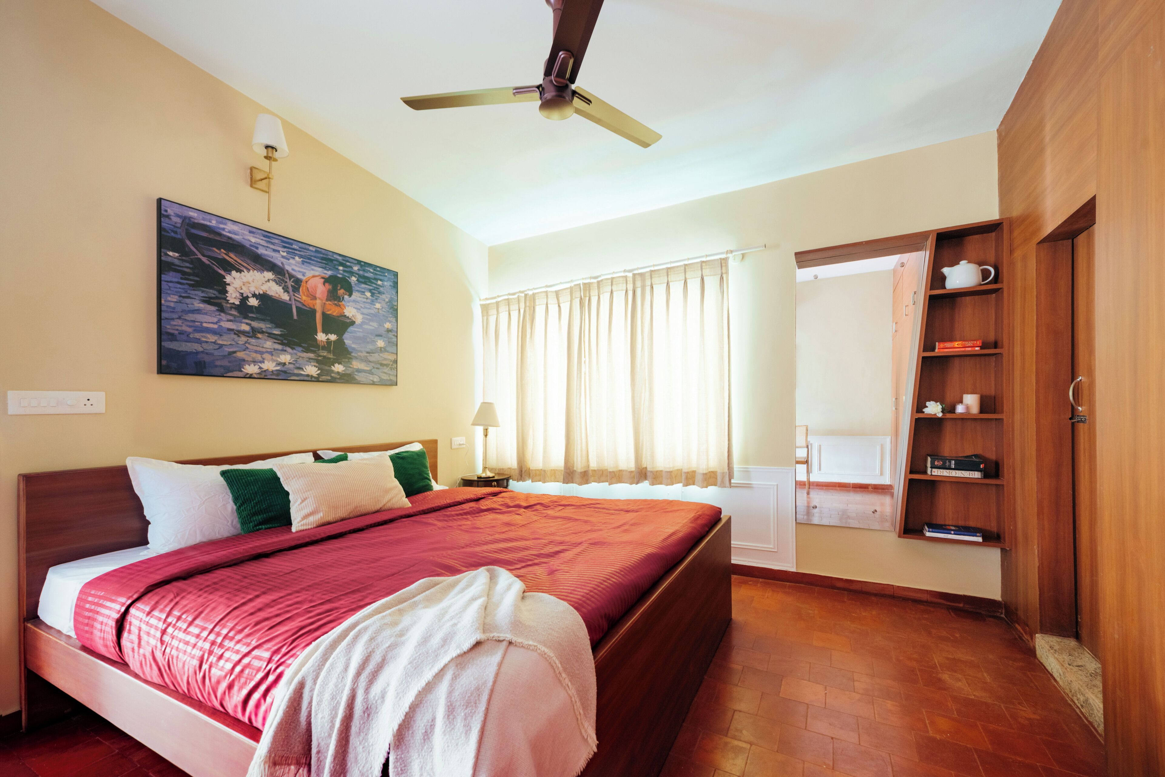Una habitació d'hotel amb un llit, un ventilador de sostre, un quadre, una finestra amb cortines i un armari de fusta.