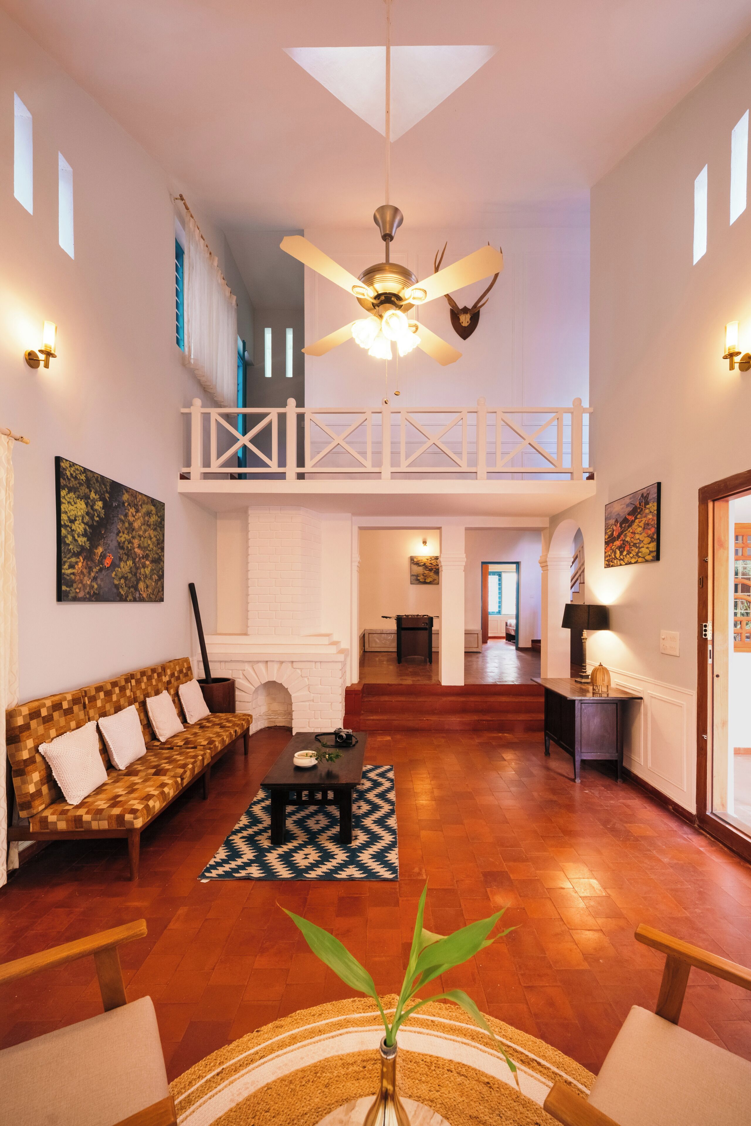 A spacious living area with a high ceiling, a ceiling fan, a fireplace, a sofa, a coffee table, and a staircase leading to an upper level.