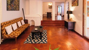 Amplia sala de estar con techo alto, ventilador de techo, chimenea, sofá, mesa de centro y escalera que conduce a un nivel superior.
