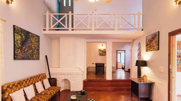 A spacious living area with a high ceiling, a ceiling fan, a fireplace, a sofa, a coffee table, and a staircase leading to an upper level.