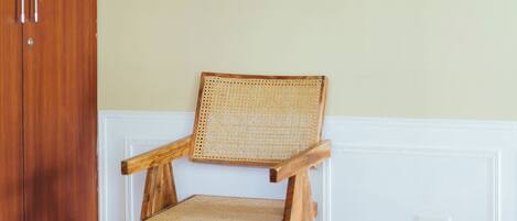 Una habitación con una silla de madera, una colcha roja, una pared blanca y un cuadro.