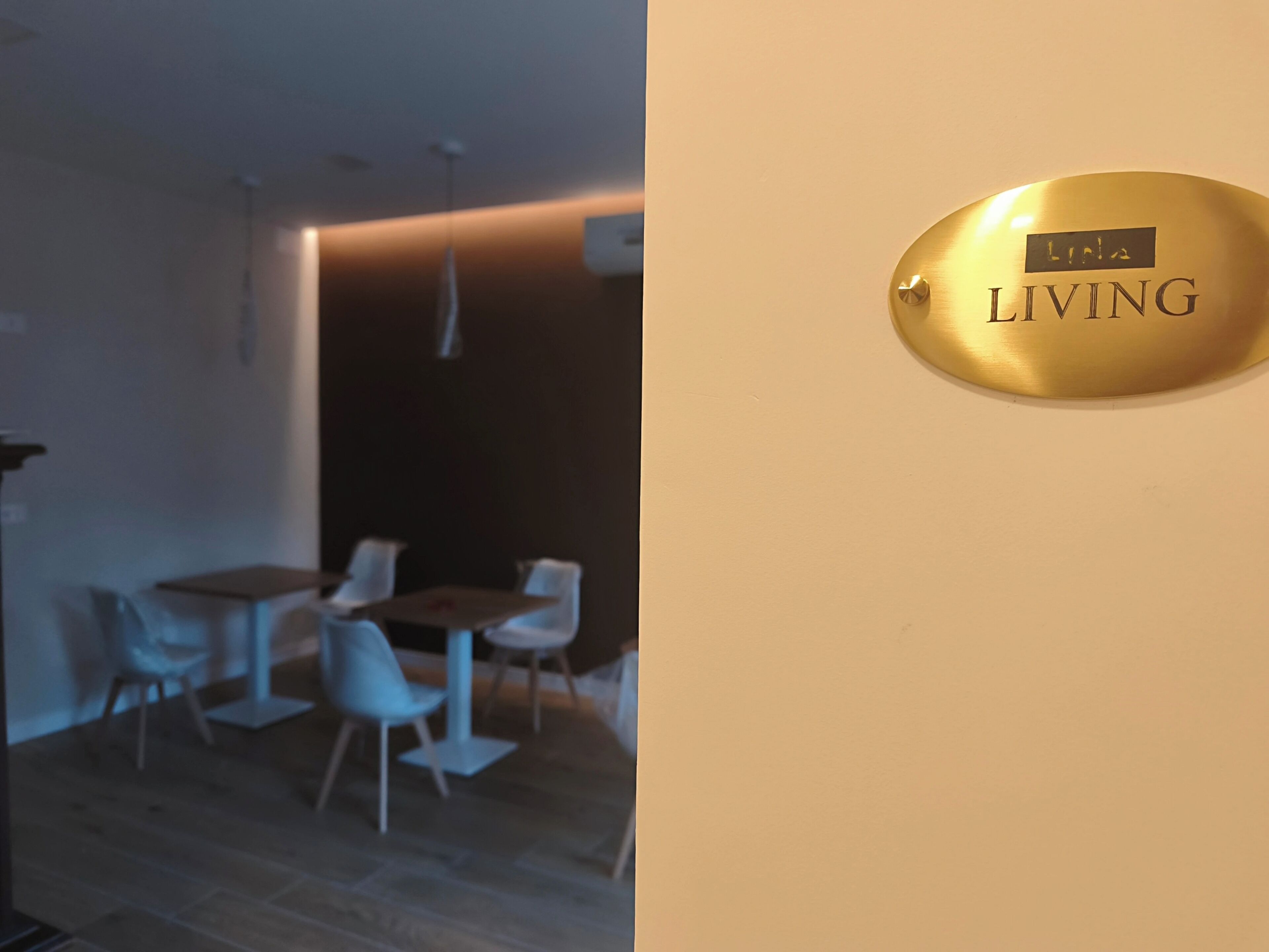 A dining area with a table and chairs, a wall-mounted light fixture, and a gold plaque with the text 'Lila Living'.