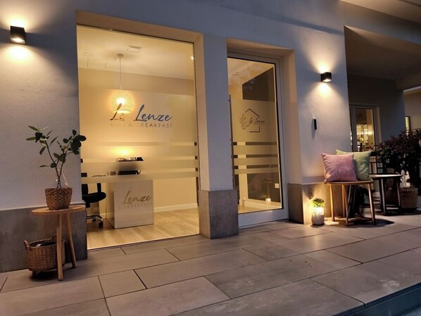 A modern cafe with a glass entrance, outdoor seating, and a minimalist interior.