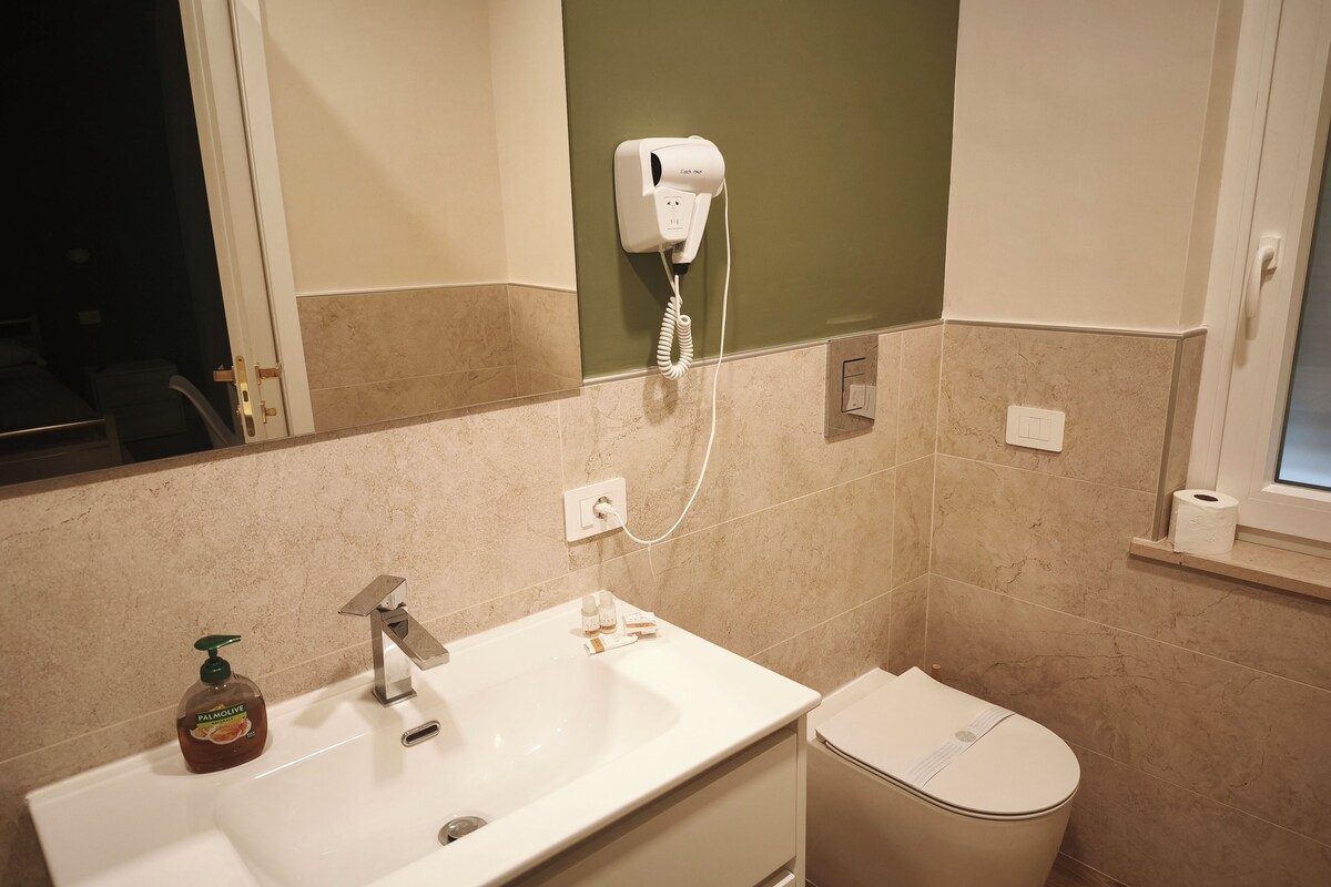 A bathroom with a sink, mirror, hairdryer, and toilet.