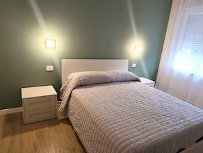 A bedroom with a bed, bedside tables, and wall-mounted lights.