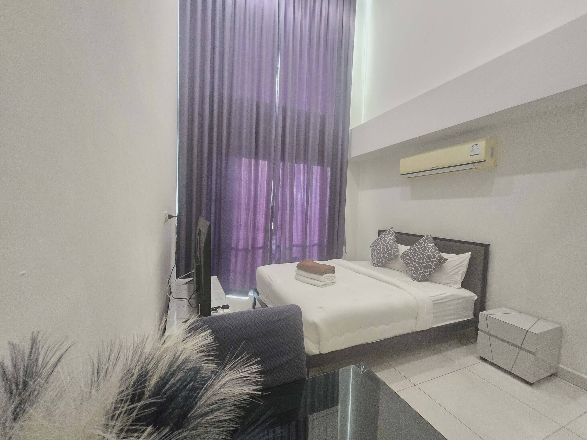 Een moderne slaapkamer met een bed, nachtkastje, airconditioning en een raam met paarse gordijnen.