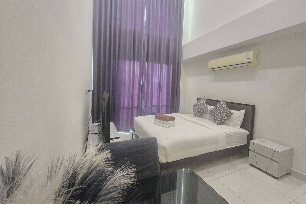 Een moderne slaapkamer met een bed, nachtkastje, airconditioning en een raam met paarse gordijnen.