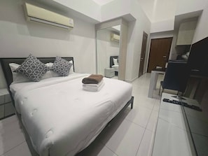 Hotellihuone, jossa on sänky, työpöytä, tuoli, ilmastointilaite ja peili.