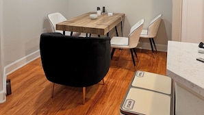Una cocina compacta con una mesa de madera, sillas blancas, una silla negra y un refrigerador de estilo vintage.