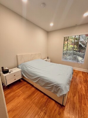 A bedroom with a bed, a nightstand, a bedside table, a window with blinds, and a ceiling light. - Furnished luxury apt, pool, sauna, great location (Los Angeles)