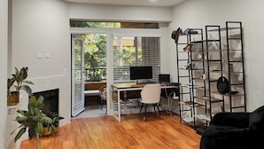 Una sala de estar moderna con piso de madera, un sofá negro, un escritorio blanco con una computadora y una estantería negra.