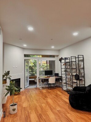 A modern living room with a wooden floor, a black sofa, a white desk with a computer, and a black bookshelf. - Furnished luxury apt, pool, sauna, great location (Los Angeles)