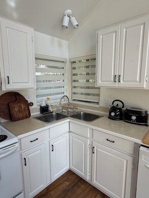 A kitchen with white cabinets, a double sink, a kettle, and a toaster.