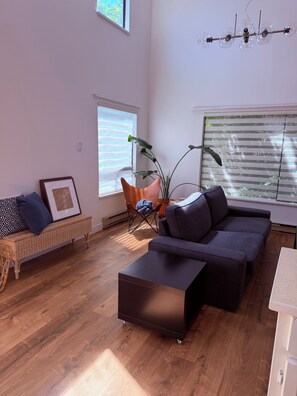 Un salon moderne avec un canapé, un pouf, un banc en osier et une plante en pot.