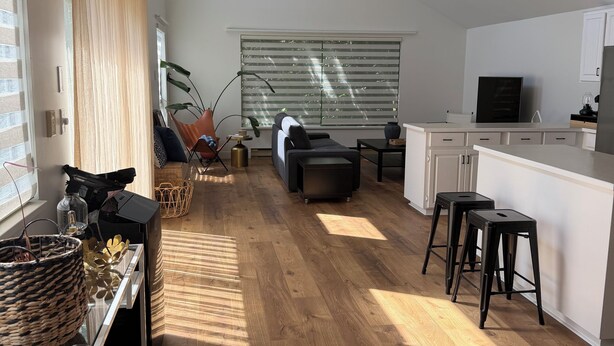 A spacious living area with a wooden floor, a sofa, a dining table, and a kitchen area with a TV.