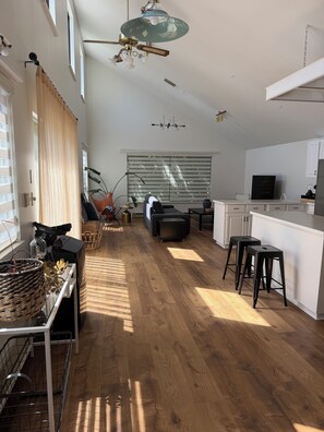 Un vaste espace de vie doté d’un plancher en bois, d’un canapé, d’une table à manger et d’un coin cuisine avec un téléviseur.