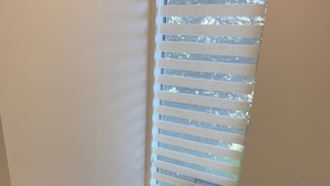 A wooden staircase with a handrail, leading to a room with a window with blinds.