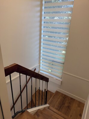 A wooden staircase with a handrail, leading to a room with a window with blinds.