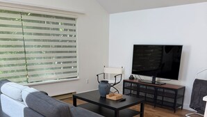 A modern living room with a sofa, a coffee table, a TV, and a window with blinds.