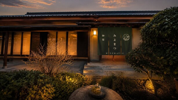 A traditional building with a sign reading 'MIYOMATSU' and a well-maintained garden with a stone lantern.