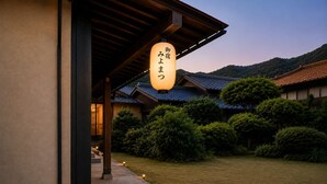 A traditional Japanese building with a sign in Japanese, surrounded by greenery and hills in the background.
