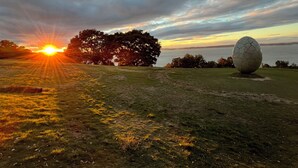 A grassy field with a large spherical sculpture and a sunset in the background.