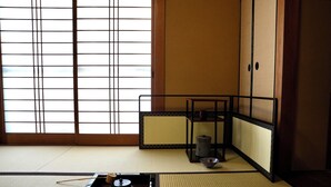 A tatami mat room with a shoji screen, a tatami mat floor, a low table with a tea set, and a traditional Japanese room divider.