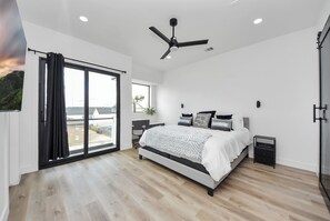 Un dormitorio con cama, ventilador de techo, escritorio, silla y una ventana grande.