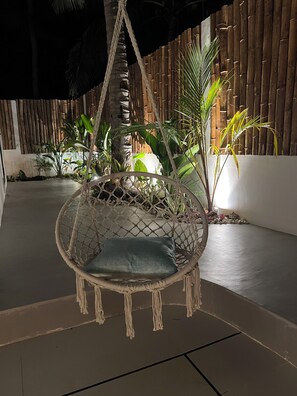A hanging chair with a cushion, surrounded by plants and a bamboo fence. - Alma Villas (San Juan)