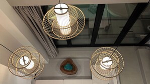 A modern interior with three circular wicker pendant lights, a white sofa with cushions, and a decorative wooden piece on the wall. - Alma Villas (San Juan)