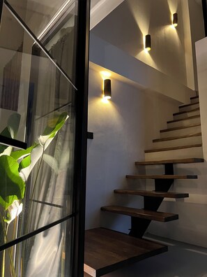 A modern staircase with wooden steps and black railings, illuminated by wall-mounted lights.