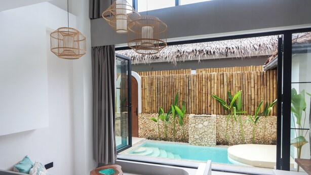 A modern bathroom with a glass shower enclosure, a bathtub, and a view of an outdoor pool area with bamboo and plants. - Alma Villas (San Juan)