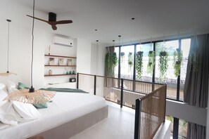 A modern bedroom with a large bed, a ceiling fan, a balcony with plants, and a view of the outdoors.