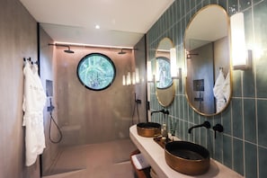 A modern bathroom with a glass-enclosed shower, two sinks with round mirrors, and a towel rack with white towels. - Alma Villas (San Juan)